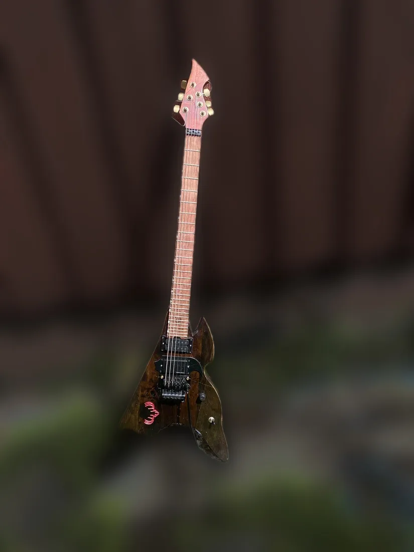 Reindeer Rifle: dark spiky V-shaped guitar with a magazine-shaped fin, leaning on a red wooden wall outdoors